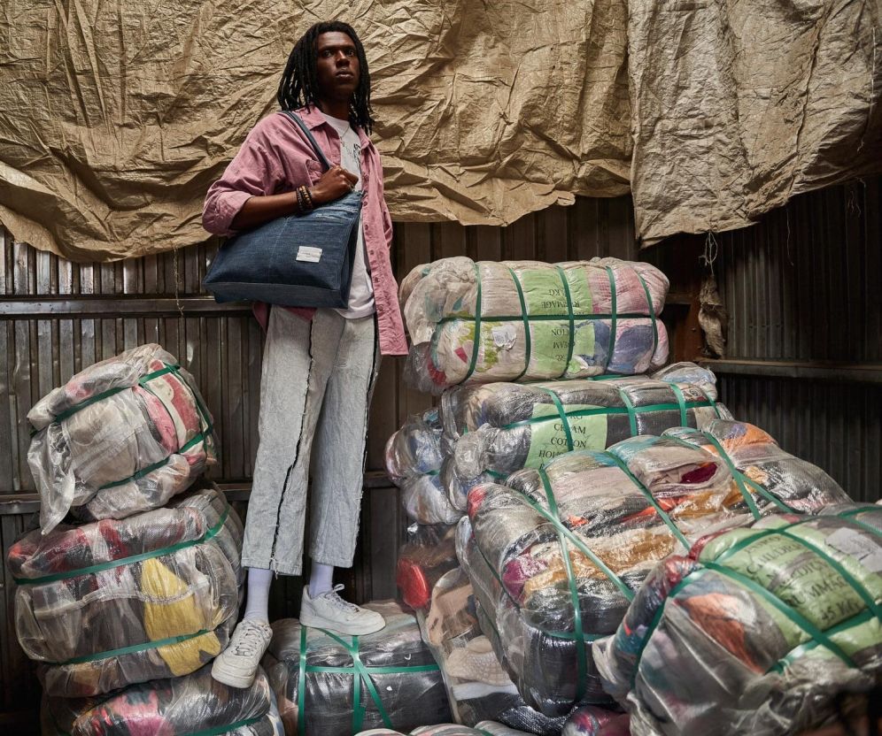 An African man standing on packaged waste holding a handbag over his shoulder. 